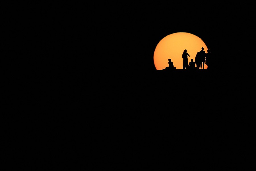 Half a dozen people in silhouette in front of the setting sun