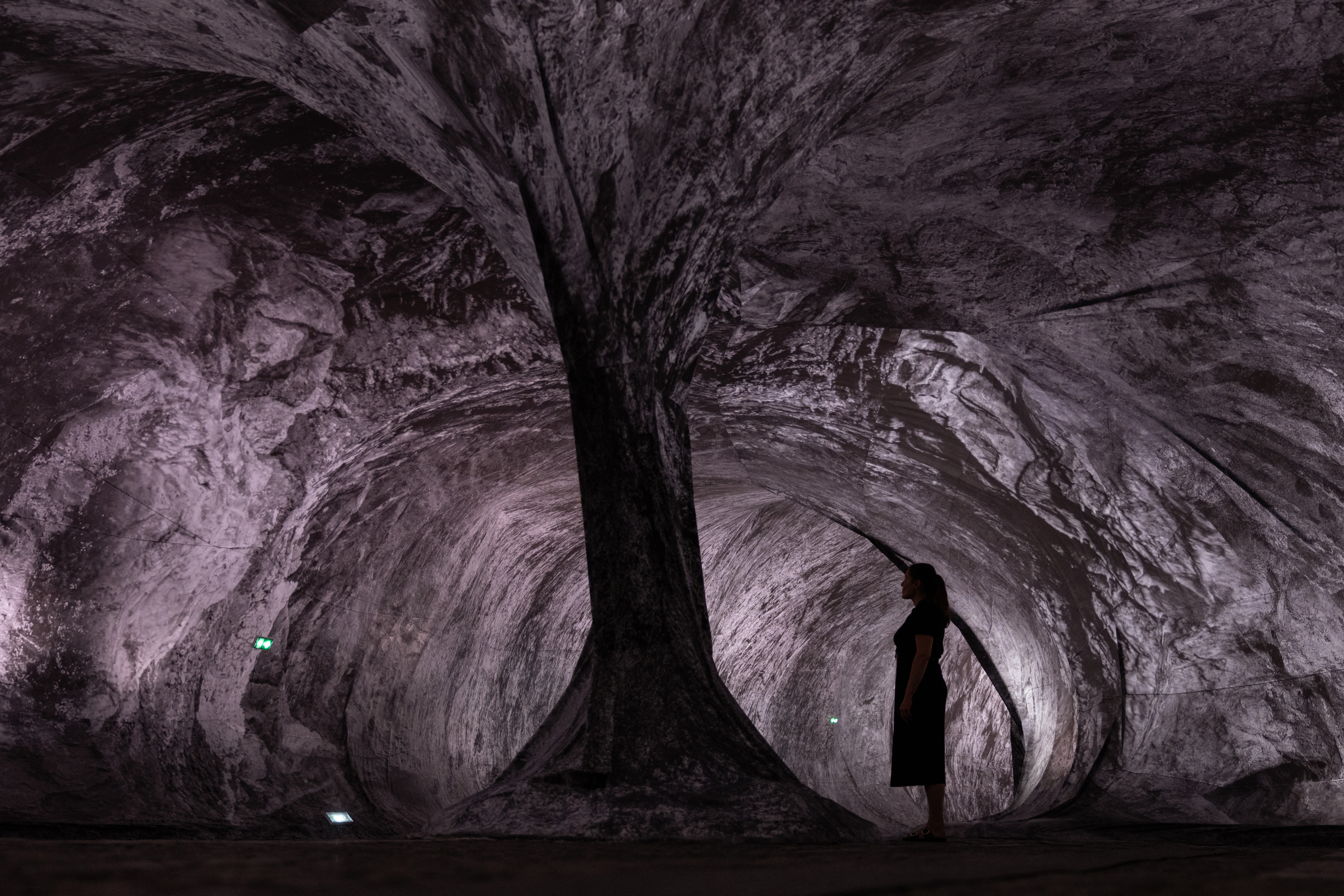 A person stands inside an art exhibit, looking up, appearing as if they were in a cave.