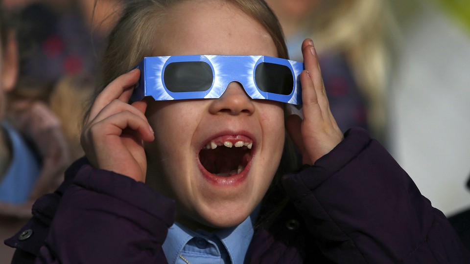 A pupil wears protective glasses as she views a partial solar eclipse from a school in Altrincham.