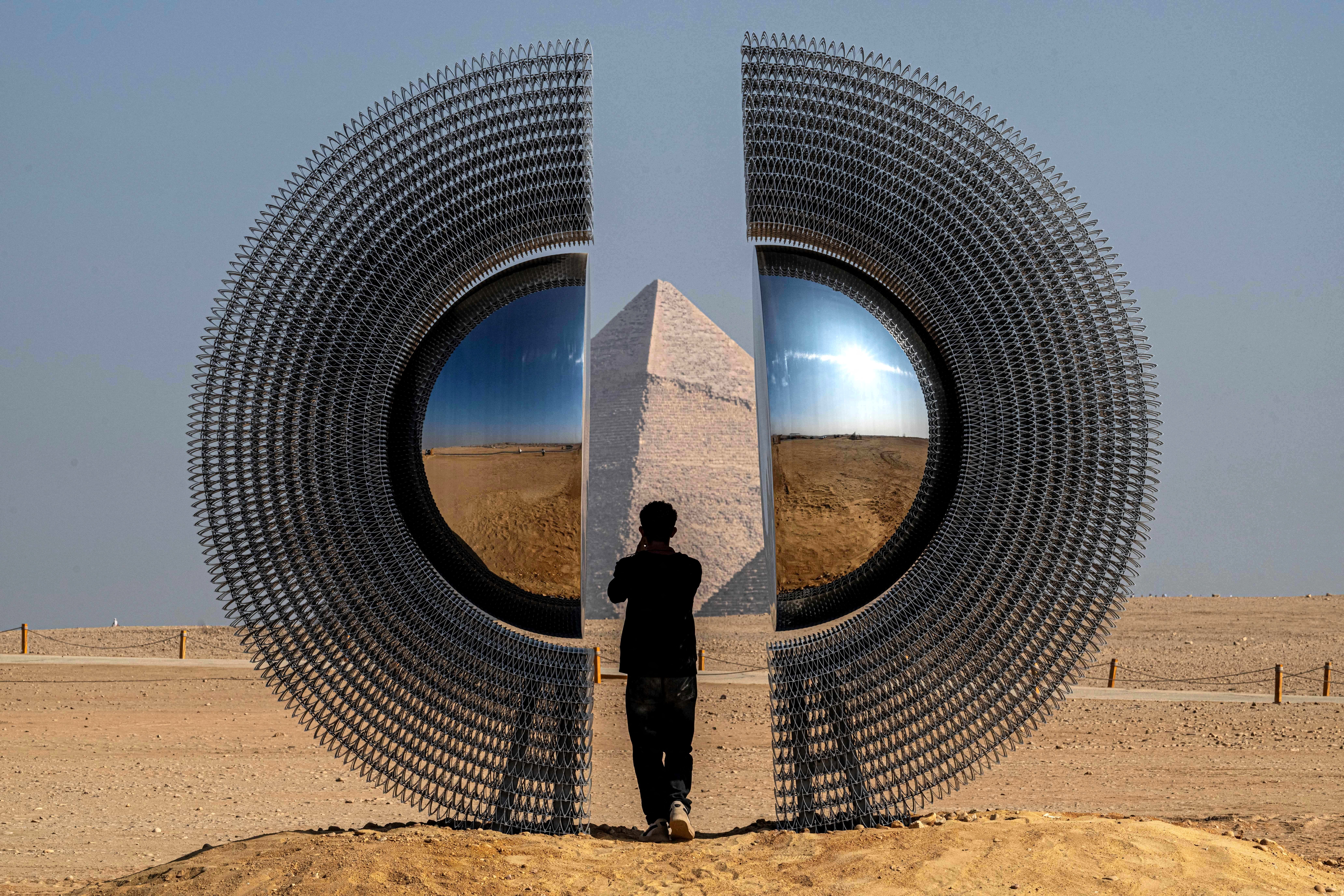 A person stands inside a large circular art installation that has been set up beside the Giza pyramids in Egypt.