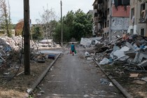 Photo of a woman walking down a road in Ukraine with debris and destroyed buildings around her.