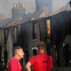 Two people stand in front of a burned building.