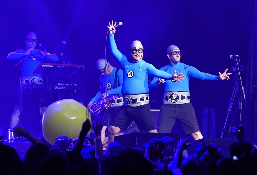 Performers in blue superhero-style costumes pose onstage.