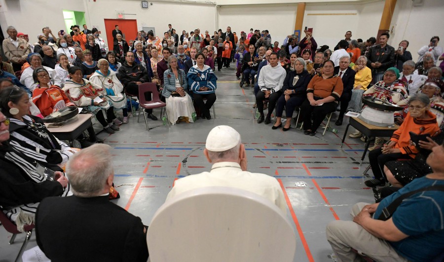 Pope Francis meets with a crowd of Indigenous people in a large room in a school.