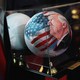 An image of a soccer ball painted with President Trump’s face and an American flag on it in a glass case titled “Ball 47”