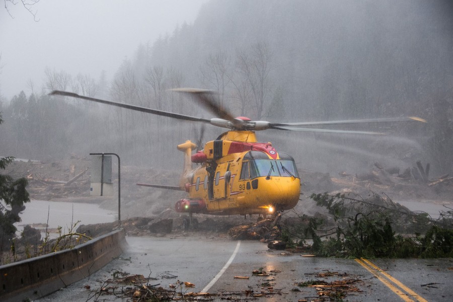 A large helicopter lands on a flood-damaged road.