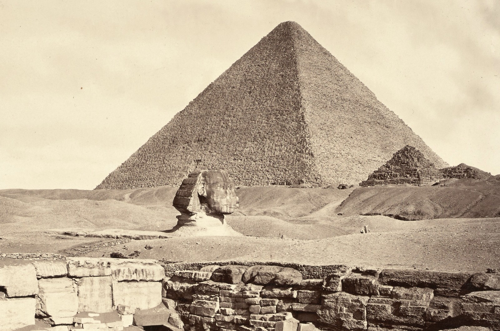 A historic photo of one of Egypt's pyramids in Giza, alongside a mostly-buried Sphinx.