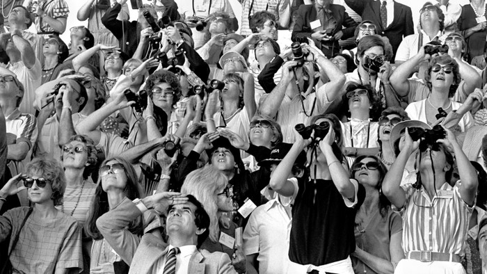 A group of people look up at the sky with binoculars