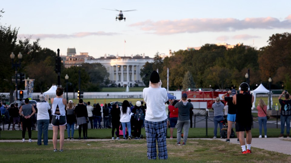 A helicopter flies over the White House as a crowd looks on