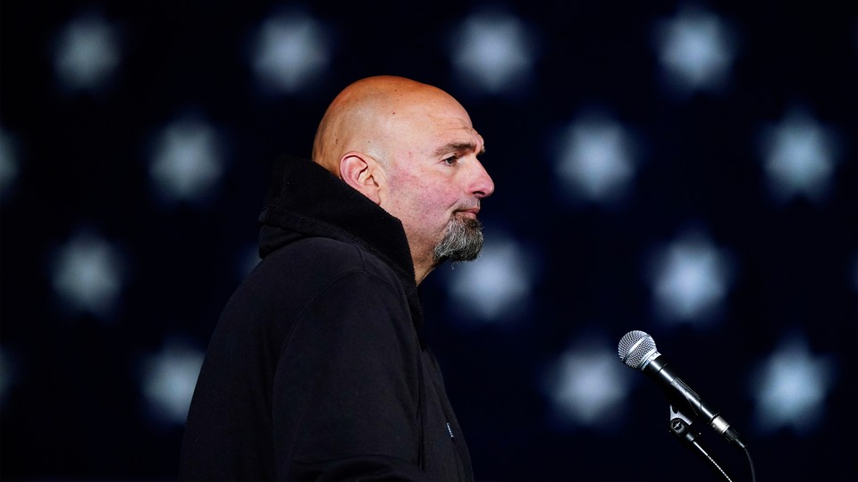 A photograph of John Fetterman in profile standing in front of a microphone