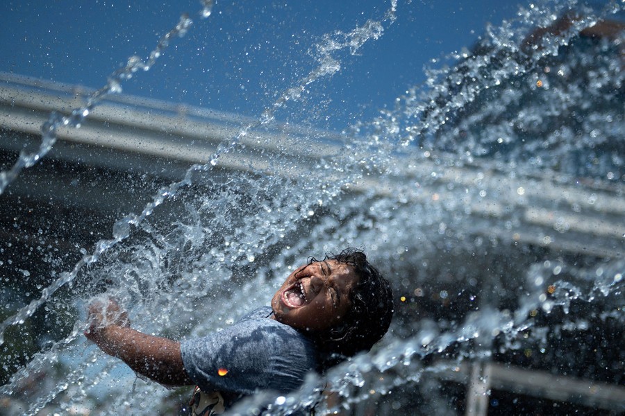 A child enjoys playing in a fountain on a hot day.