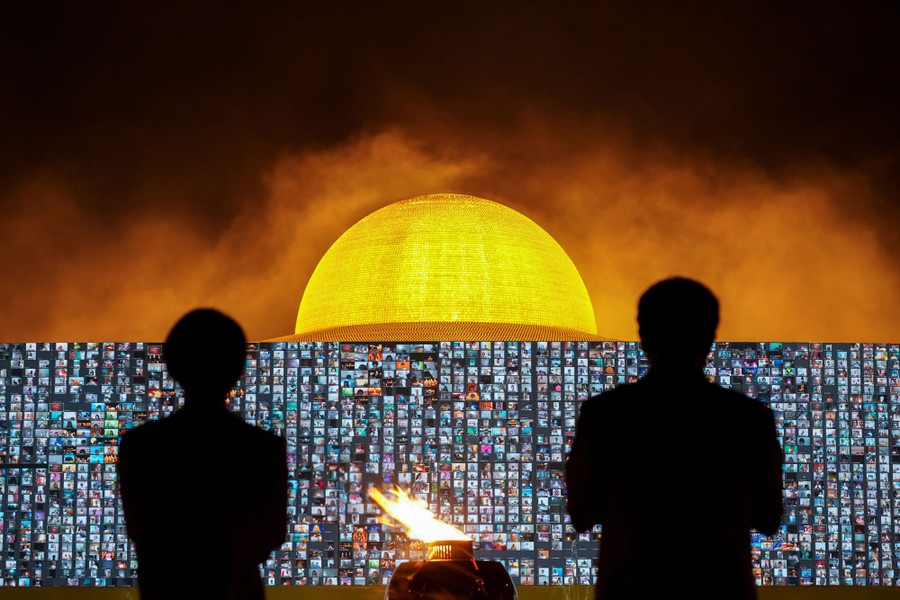 People pray at a temple, in front of a video screen filled with hundreds of faces.