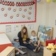 Photograph of a teacher sitting on the floor of a colorful classroom, reading to two children.
