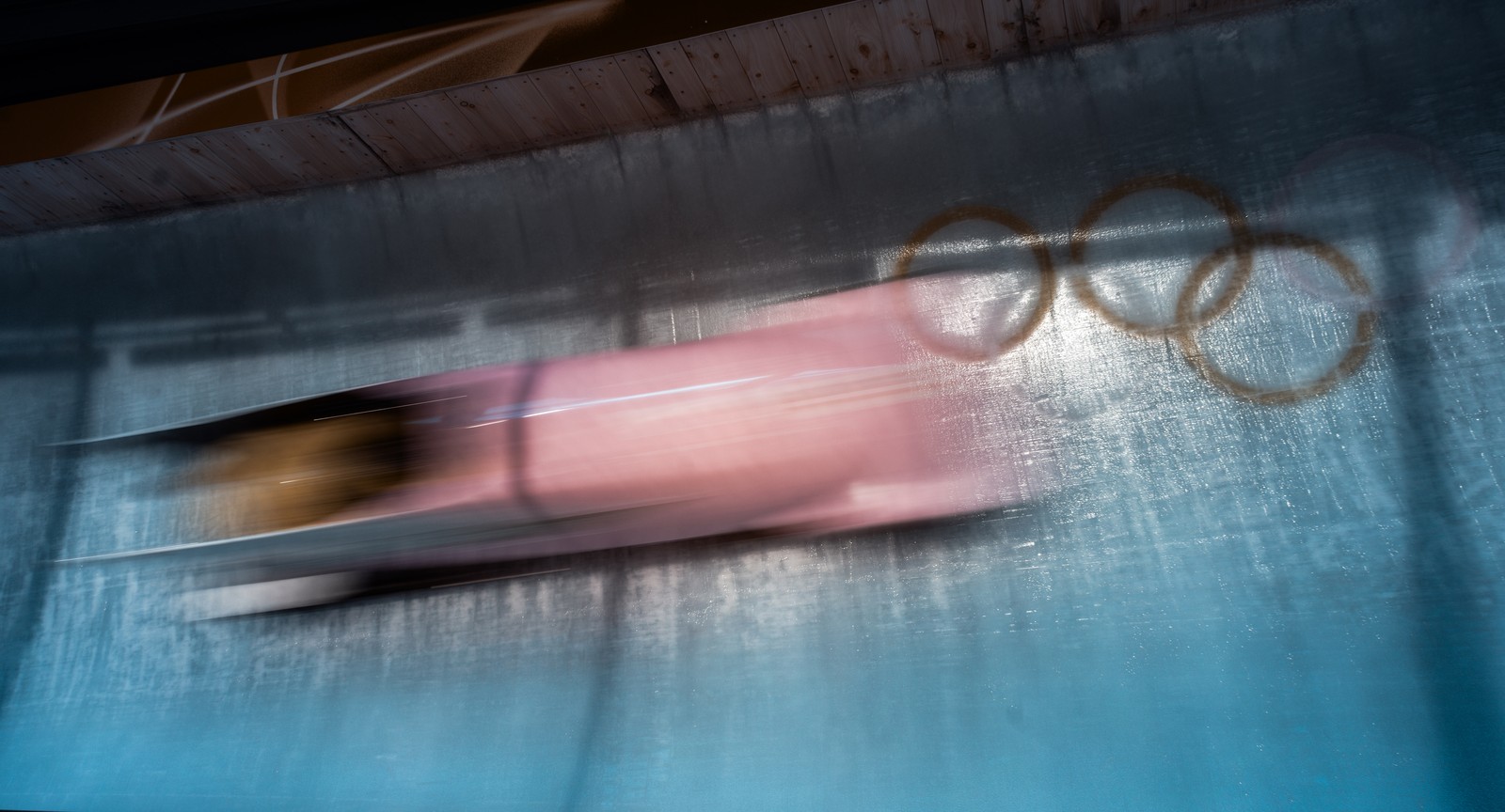A bobsleigh rushes past on an ice track, seen as a blur, in an image featuring filtered colors.