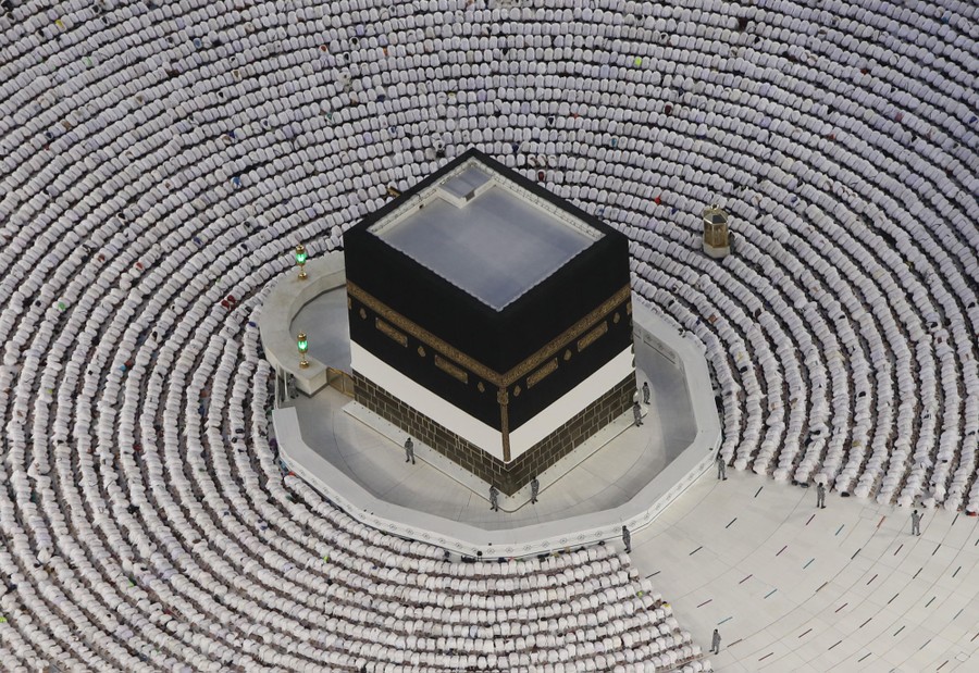 Hundreds of kneeling pilgrims encircle a black cube-shaped building.