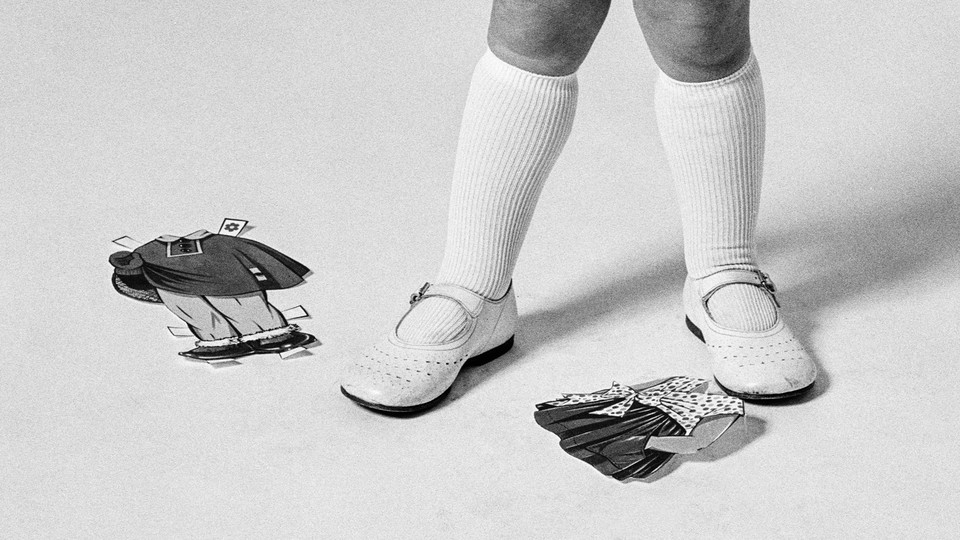 A black-and-white photo of a children's feet next to two paper-doll costumes—one traditionally male, the other female