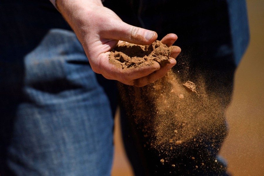 A person crumbles dry earth in their hand.