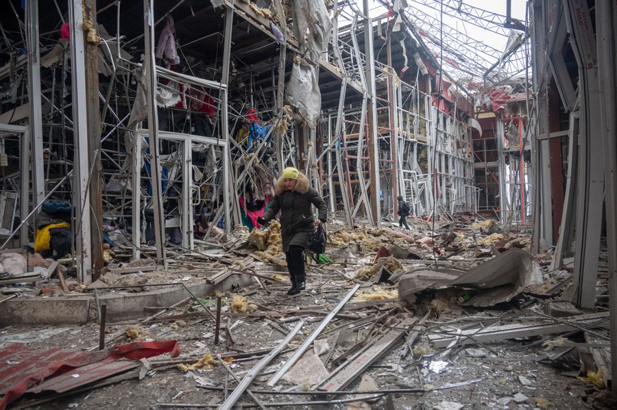 Two people pick their way through debris, walking past heavily bomb-damaged storefronts in a mall.