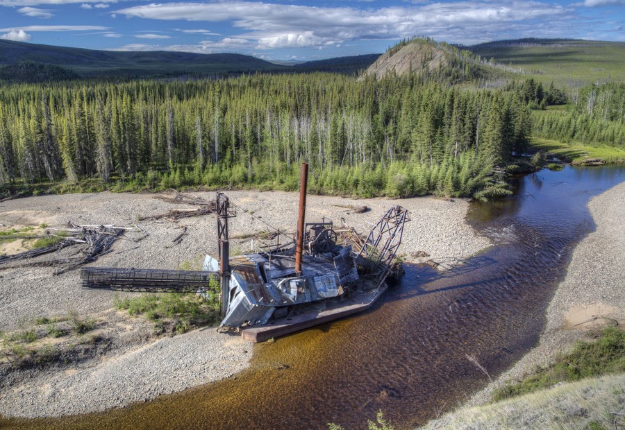 Wreckage of an old gold-mining dredge lies beside a river.