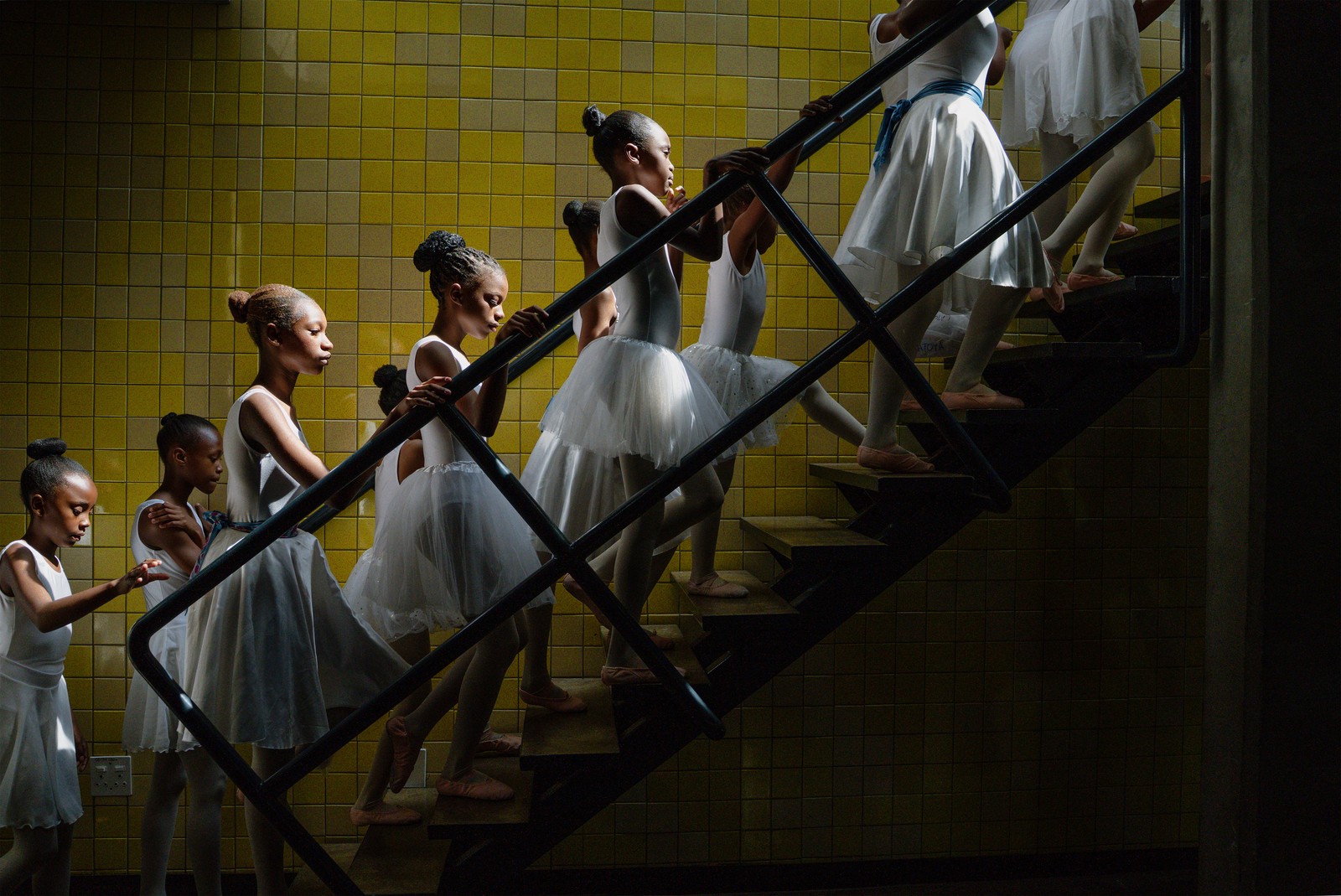A group of young ballet dancers ascend a staircase.