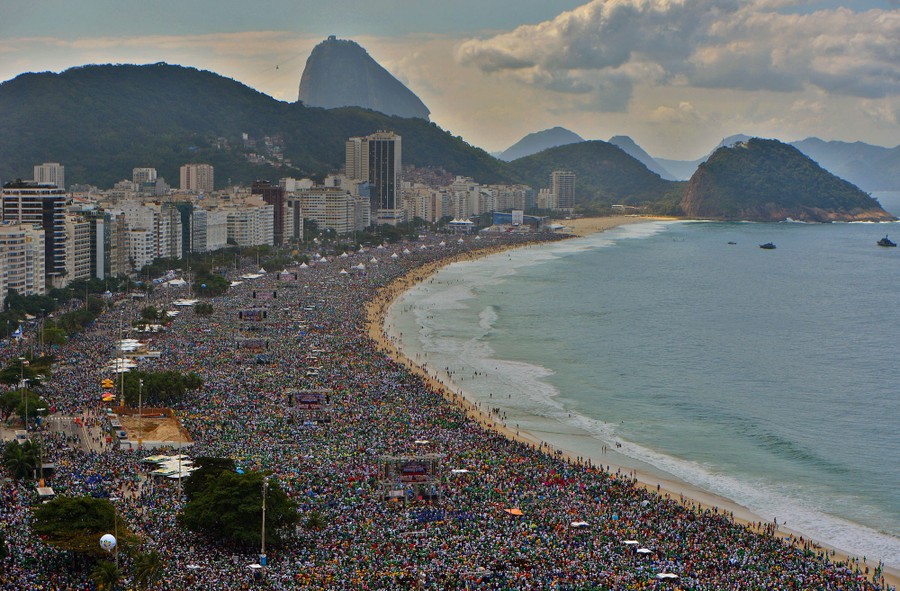 An elevated view of a wide beach in Rio de Janeiro, completely packed with thousands of people.