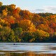 A person sits in a canoe on a lake surrounded by fall-colored trees.
