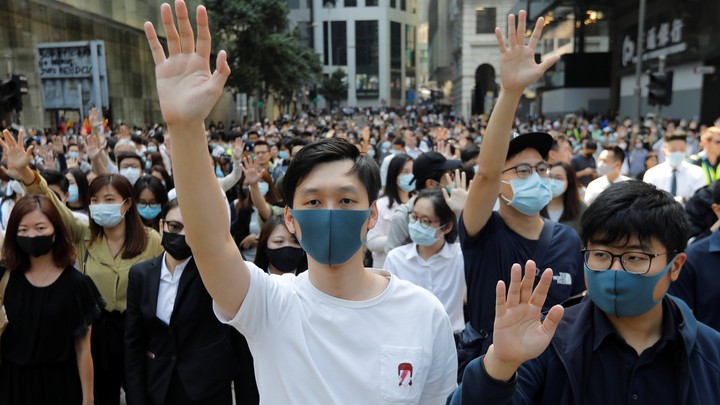 A crowd of Hong Kong protesters in masks raise their hands in unison.