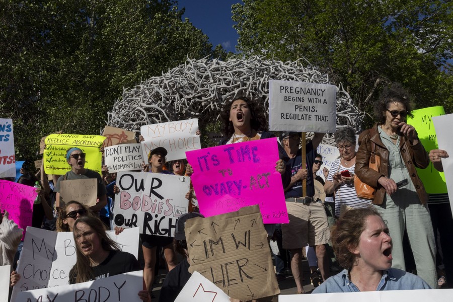 Protesters hold signs and chant slogans in front of an arch made of elk antlers.