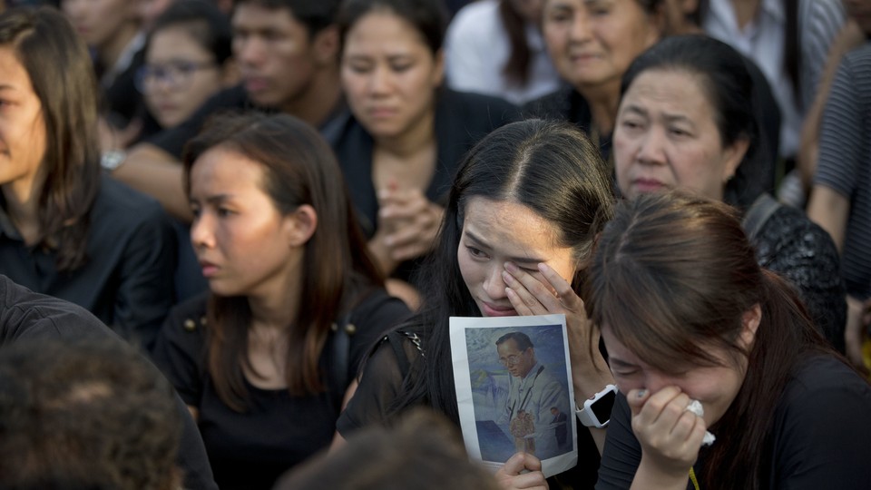 A Thai woman wipes away tears as she holds a picture of the late King Bhumibol Adulyadej.