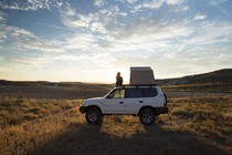A woman standing by a car, looking out at a view