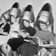 A group of women sit underneath hair dryers and read magazines at a hair salon.