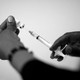 A photo of two hands filling a syringe with a vaccine