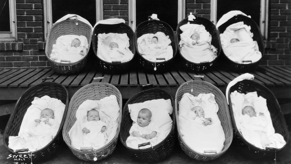 Ten babies, all but one sleeping, rest in baskets on a porch outside a maternity ward.