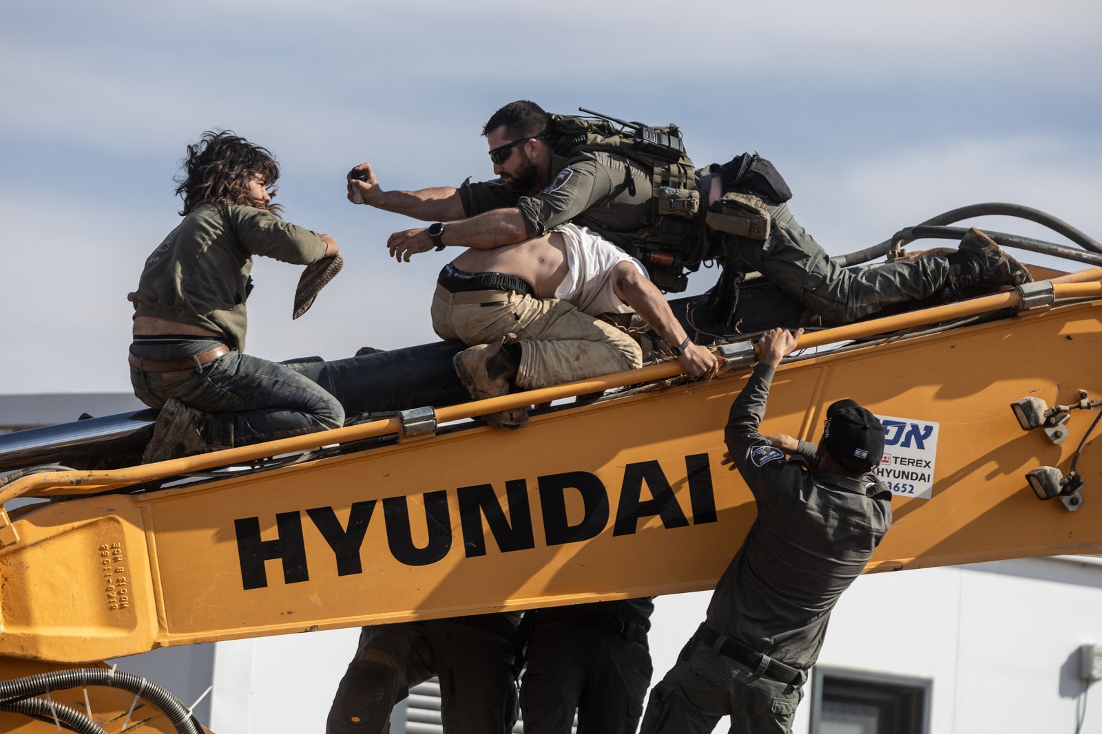 Several soldiers struggle with civilians atop the long arm of a piece of construction equipment.
