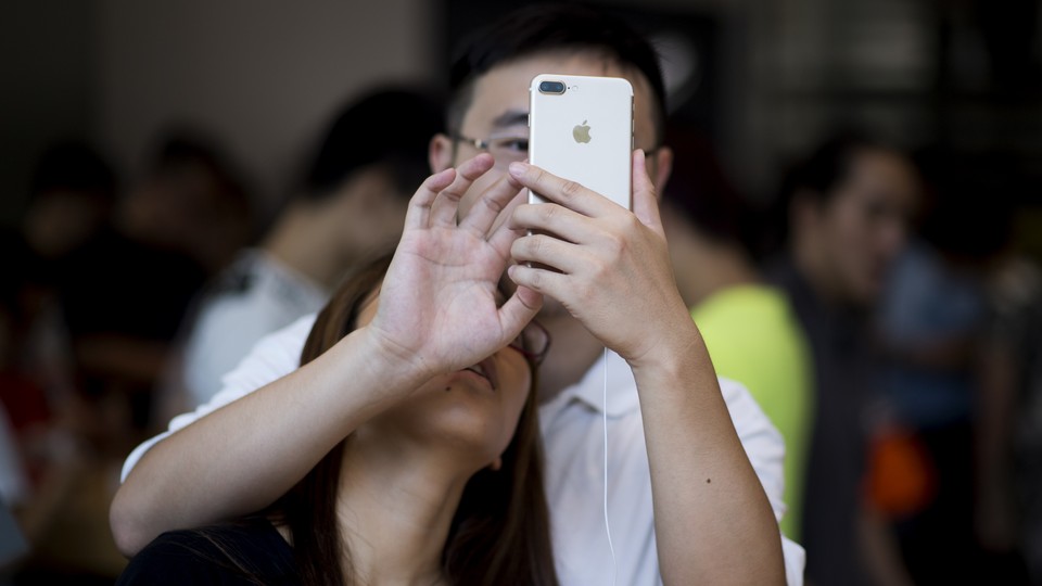 A woman leans on a man's shoulder, looking up on a phone in his hand