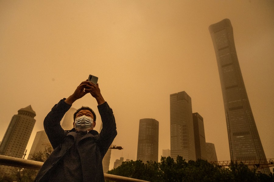 A man takes a selfie in front of skyscrapers during a dust storm.
