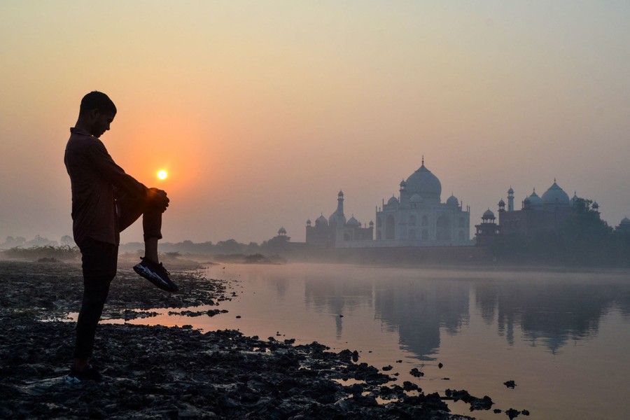 A boy exercises on the banks of a river near the Taj Mahal at sunrise.