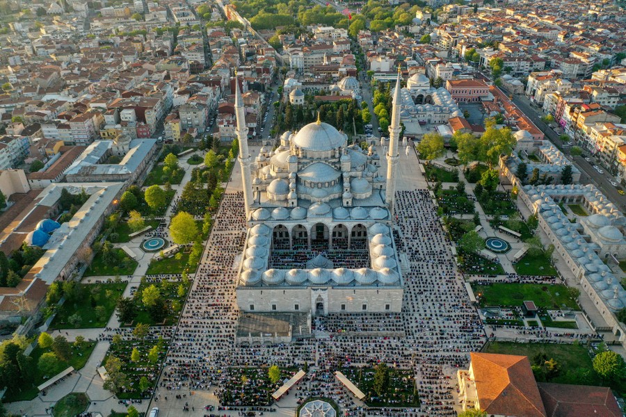 An aerial view of a large mosque, with hundreds of worshippers inside and out.