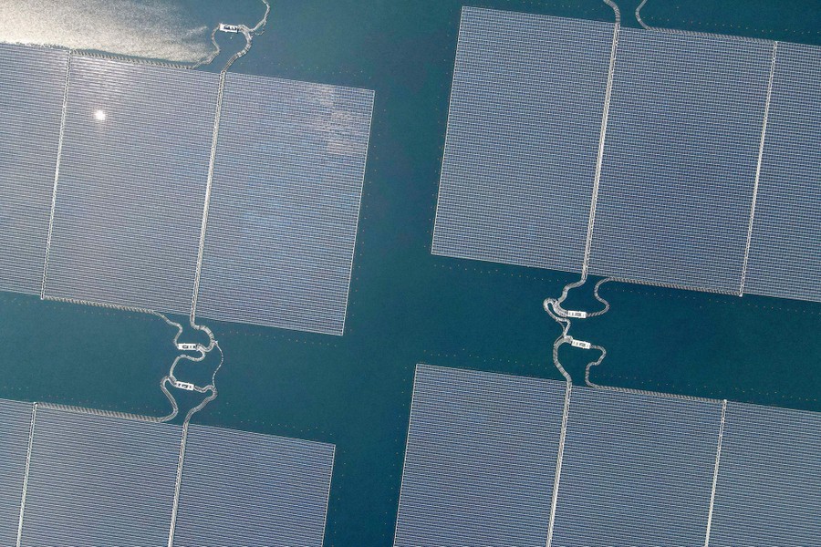 An aerial view of several large arrays of solar panels floating on a reservoir's surface