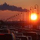 Pipes of a thermal power plant are seen during sunset, with cars stuck in a traffic jam in the foreground.