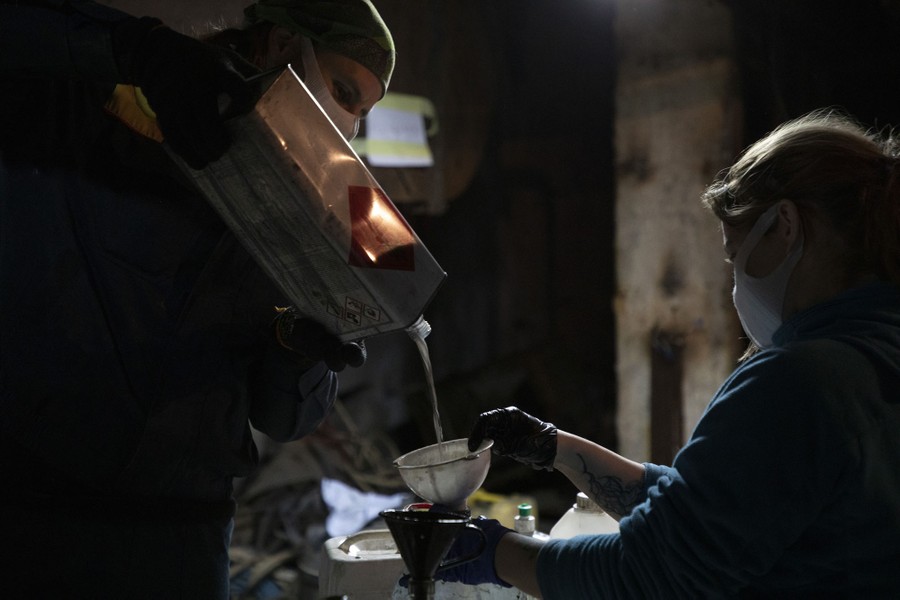 A person pours liquid from a metal canister into a funnel being held by another person.