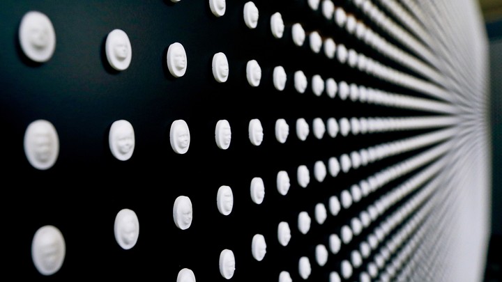A black wall displays flat white pills with faces carved into them.