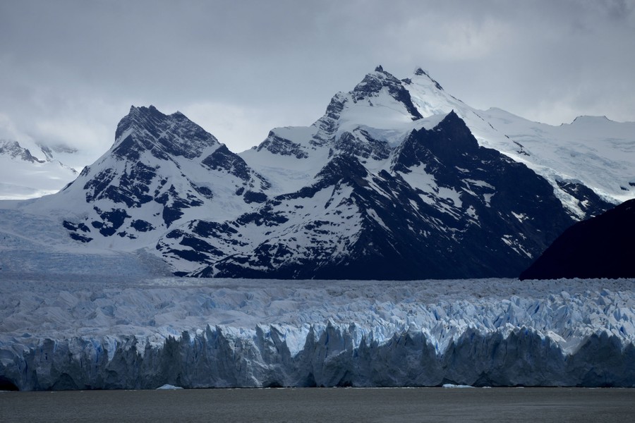 A view of a large glacier with snow-covered mountains in the background.