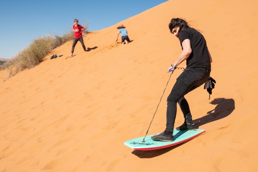 Several people play on the side of a large sand dune.