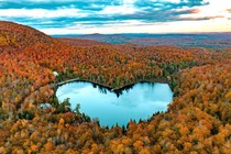 An aerial view of forested hills showing autumn colors, with a heart-shaped lake in the center.
