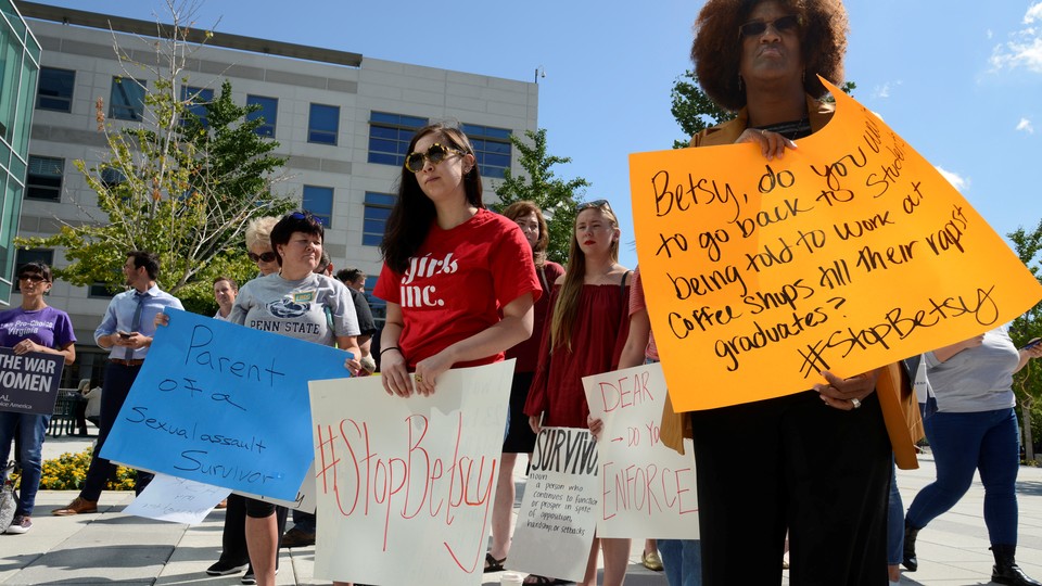 Protesters gather at a university with signs protesting Betsy DeVos and her plans for campus sexual-assault policies.