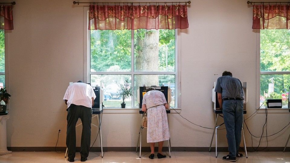 Three people filling out ballots in front of a window; trees visible through the window