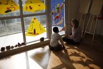 A child and adult sit together on the floor, playing with construction-paper dinosaurs.