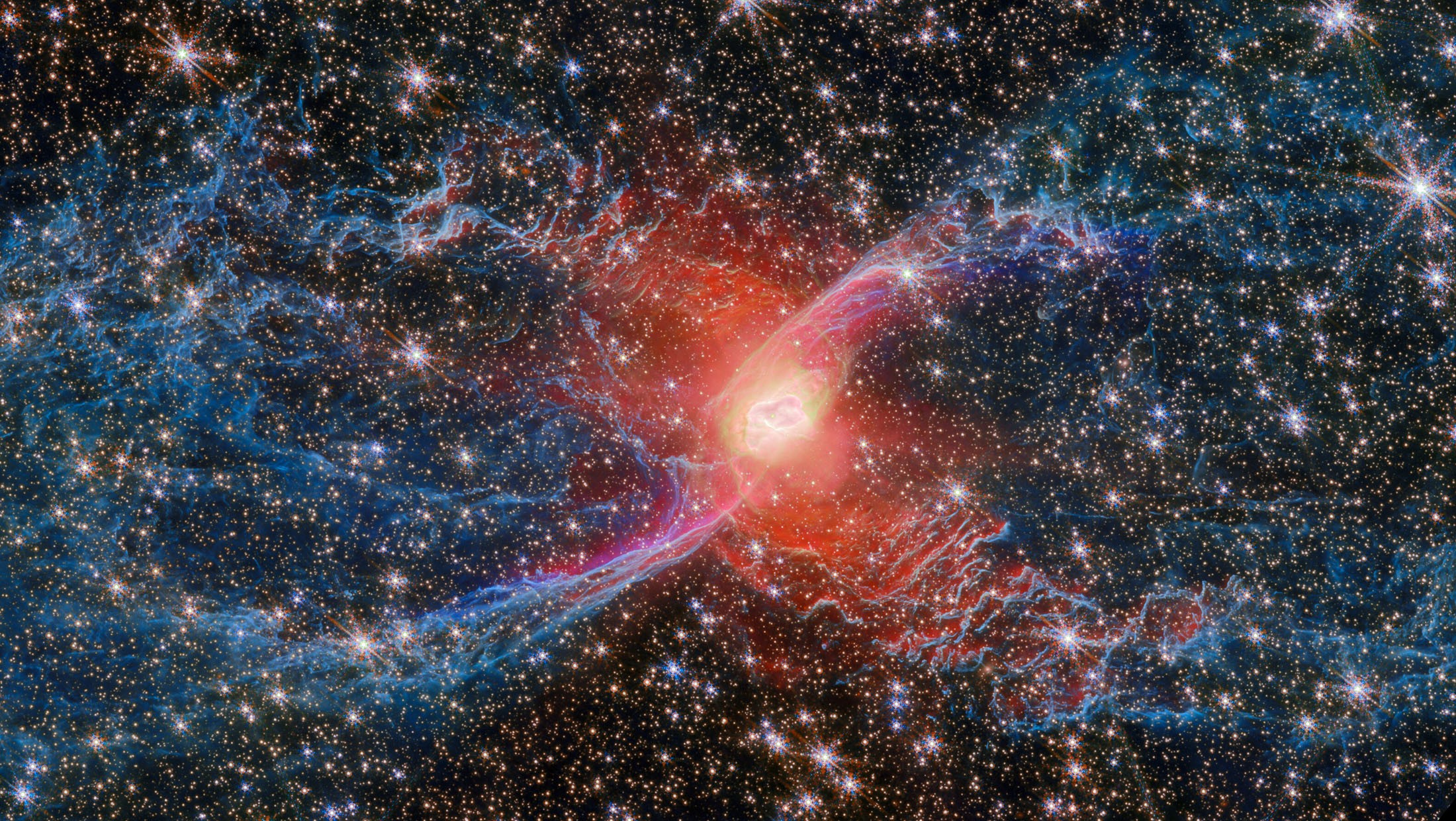 A bright red cloud appears at the center of a roughly spider-shaped trail of gas and dust, backdropped by many other stars.
