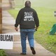 A voter walks past signs at a voting location, wearing a jacket that says, "Jesus saved my life"